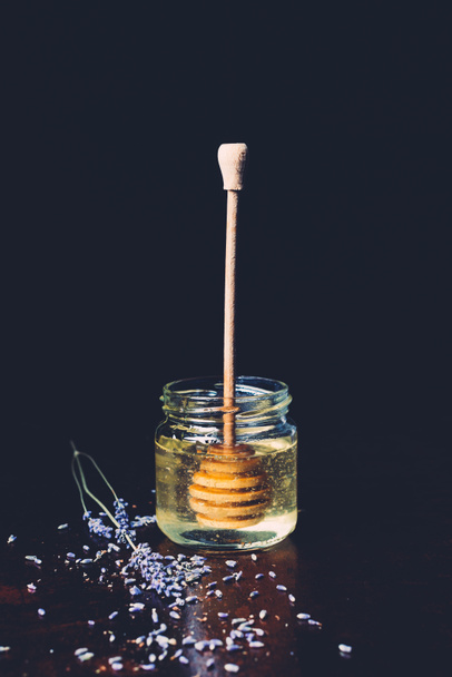 enfoque selectivo de tarro con palo de miel y pétalos de lavanda sobre fondo negro
  - Foto, Imagen