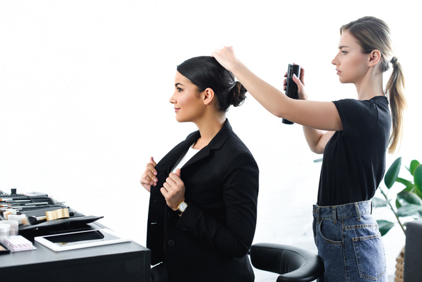 side view of businesswoman getting hairstyle fixated with hair spray by hairstylist - Foto, afbeelding