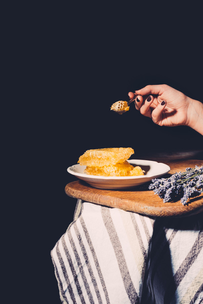 cropped image of woman holding spoon with honeycomb over table on black background  - Foto, Imagen