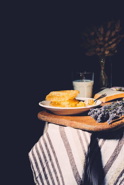 selective focus of glass of milk, honeycombs and lavender on table on black background - Photo, Image