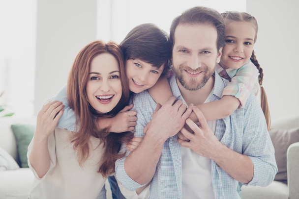 Portrait of lovely beautiful four people, mom and dad carrying on back two kids wearing casual outfit enjoying free time indoor. Trust support understanding concept - Фото, изображение
