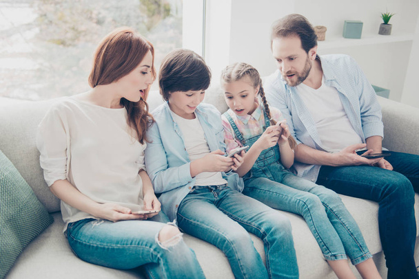Portrait of attractive family sitting on sofa in casual outfit, mom sister and dad looking in son's smart phone with astonished impressed reaction. Social networks online connection internet concept - Fotoğraf, Görsel