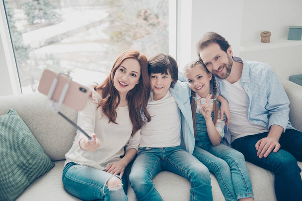Portrait of friendly bloggers mom dad two kids sitting on sofa using smart phone gadget monopod shooting selfie in front camera gesturing v-sign peace symbol with two fingers having video-call - Photo, Image