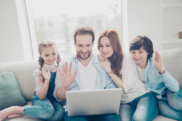 Portrait of joyful friendly family with two kids having laptop speaking with grandmother on web camera making greetings gesturing palm hi sign sitting on couch enjoying time together - Foto, Bild
