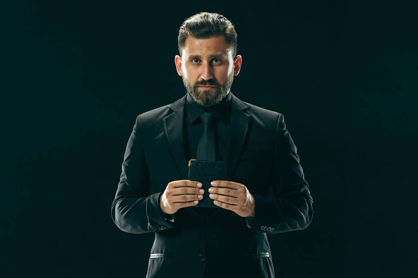Male beauty concept. Portrait of a fashionable young man with stylish haircut wearing trendy suit posing over black background. - Фото, изображение