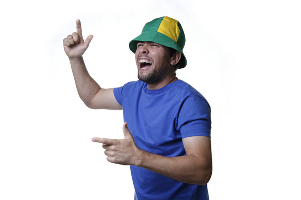 Молодой человек в синей блузке и зеленой и желтой шляпе болеет за бразильский футбол - Футбольный фанат - Счастье и энтузиазм
 - Фото, изображение