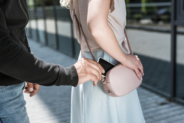 levágott nézet bűnügyi ember pickpocketing smartphone-ból womans táska utca - Fotó, kép