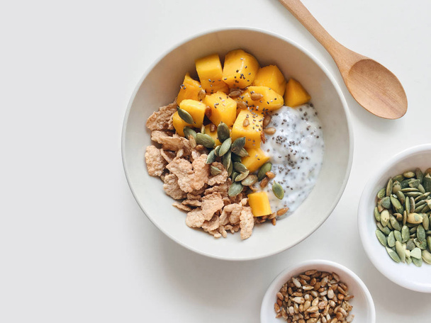 Sağlıklı kahvaltı kaseyle chia tohum puding, mango, tahıl, kabak çekirdeği ve Ayçiçeği tohumları üzerinde bir mutfak masa, beyaz arka plan Üstten Görünüm - Fotoğraf, Görsel