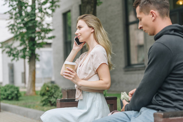 hombre carterista dinero de la cartera mientras que la mujer habla en el teléfono inteligente y beber café en el parque
   - Foto, imagen