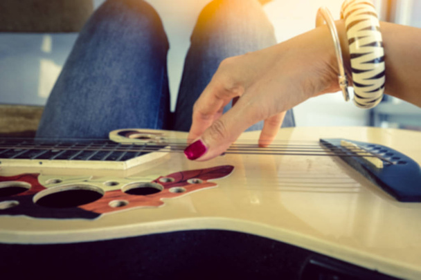 Blurred image of woman fingers playing guitar relaxing at home in vintage style  - Fotó, kép