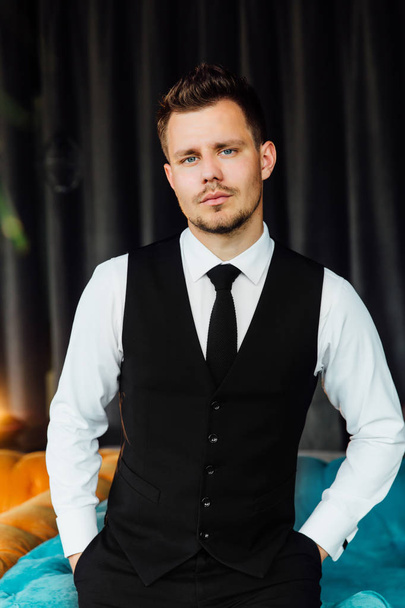 Stylish athletic man in a business costume vest. Sits in the turquoise sofa chair, a serious look. - Valokuva, kuva