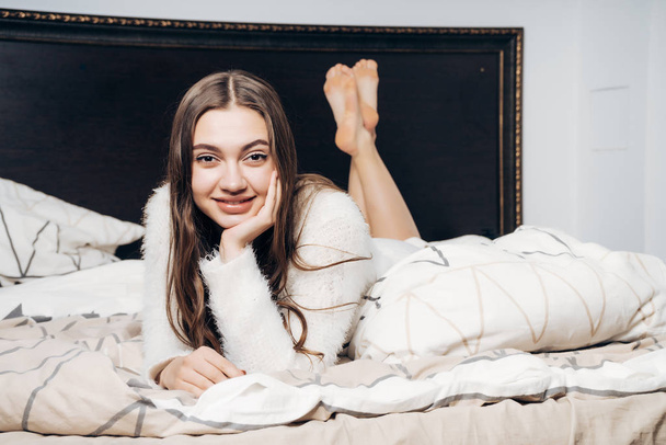 beautiful charming girl in pajamas lies in bed in the evening, resting after a hard day's work and smiling - Fotó, kép