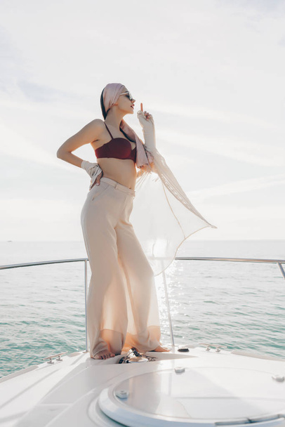a luxurious stylish girl in fashionable summer clothes posing on a yacht, enjoying vacations and the sea - Foto, Imagen