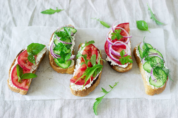 Bruschetta or sandwiches with tomatoes, cucumbers and cream cheese, decorated with greens. - Valokuva, kuva