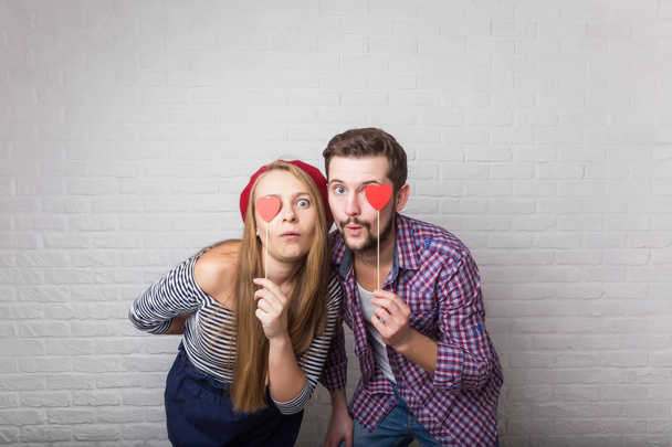 A happy funny couple in love enjoys Valentine's Day. A man with a beard and a woman with blond long hair. Paper red hearts. Loft style. - Foto, Imagen