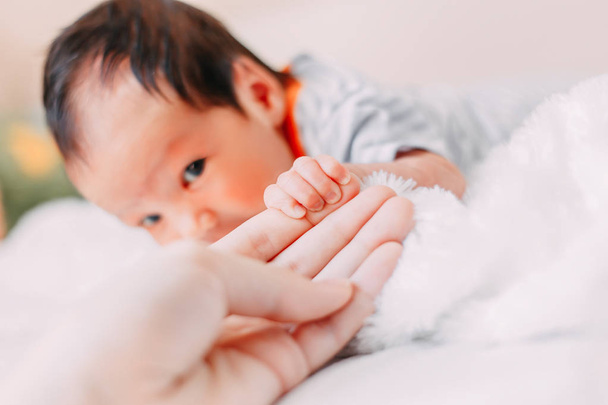 Nahaufnahme der kleinen süßen Hand des Babys, die nach der liebevollen Hand der Mutter greift. während sie ihren Finger hält, streichelt sie seine Hand. - Foto, Bild