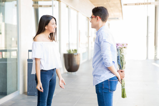 Teenager versteckt Blumen hinter Rücken für Freundin auf Flur in Einkaufszentrum - Foto, Bild