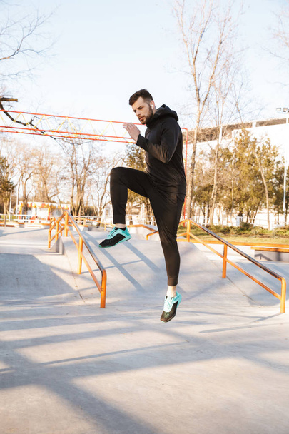 Portrait of healthy young sportsman in earphones doing exercises outdoors - Photo, image