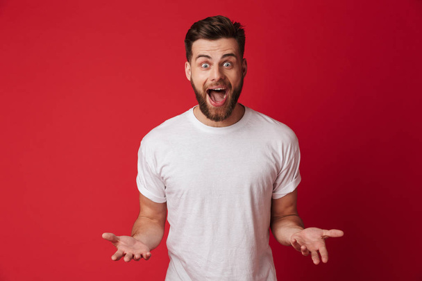 Picture of shocked young handsome man standing isolated over red wall background. Looking camera. - Foto, imagen