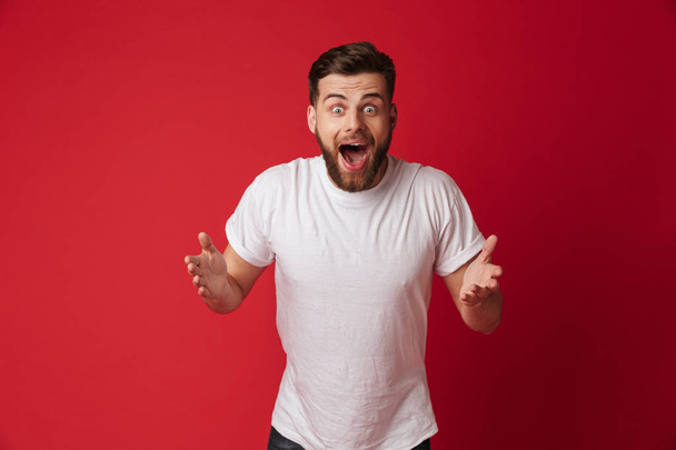 Picture of shocked young handsome man standing isolated over red wall background. Looking camera. - Foto, Imagem