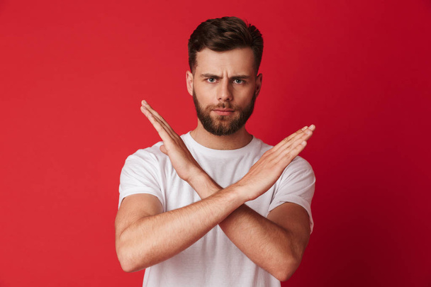 Image of serious young man showing stop gesture standing isolated over red wall background. - Foto, Bild