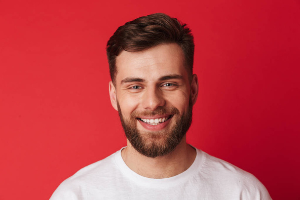 Image of handsome cheerful young man standing isolated over red wall background. Looking camera. - Foto, afbeelding