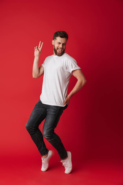 Photo of handsome young man dancing isolated over red wall background showing peace gesture. - Zdjęcie, obraz