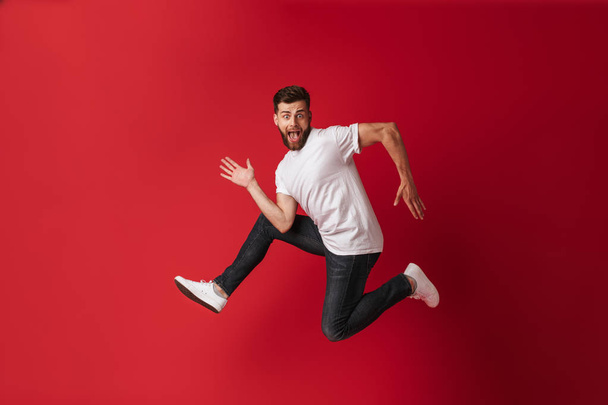 Photo of handsome excited young man running isolated over red wall background. - Foto, Imagem