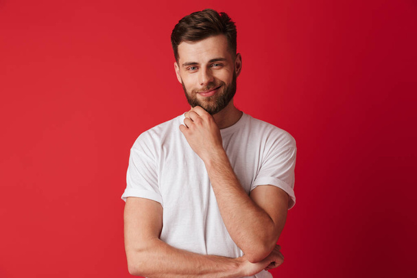 Image of handsome young smiling man standing isolated over red wall background. Looking camera. - Φωτογραφία, εικόνα