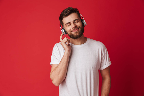 Photo of handsome young man isolated over red wall background listening music with headphones. - Valokuva, kuva