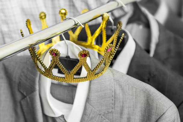 Fato de negócios com uma coroa de ouro pendurada num cabide. A roupa é uma pessoa de sucesso. Conceito de negócio. Metáfora
 - Foto, Imagem