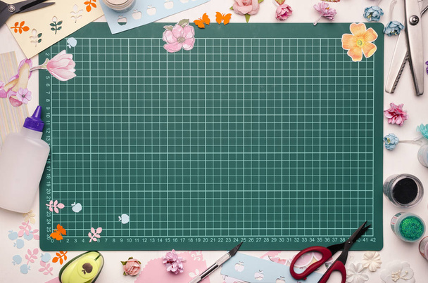 The cutting mat is surrounded by paper flowers, paper, tools and scrapbooking materials. Scrapbooking, top view - Photo, Image