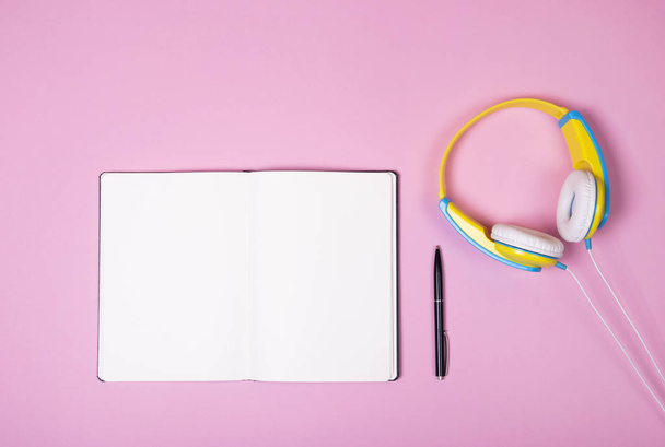 Cuffie blu e gialle, notebook aperto e penna su sfondo rosa con spazio per la copia
. - Foto, immagini