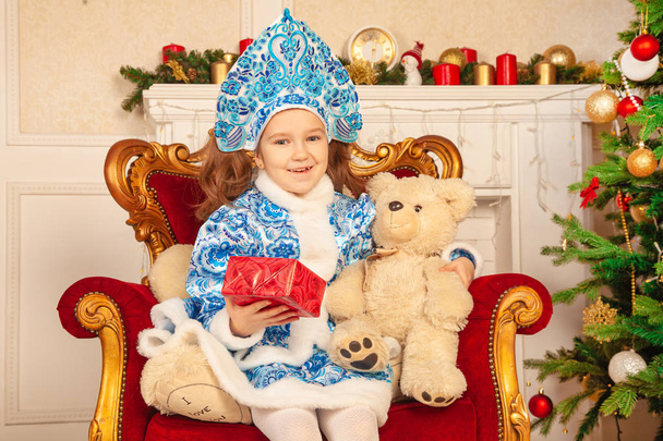 gentille fille douce enfant dans une robe bleue avec un kokoshnik sur sa tête posant près du sapin de Noël avec des cadeaux
 - Photo, image