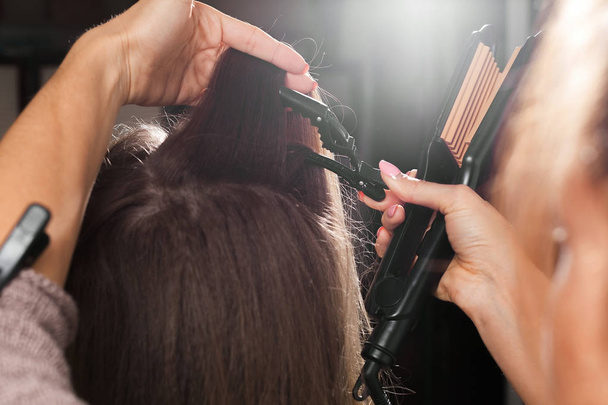 professional hairdresser clipping hair of a young model with a hairpin before making a gauffer hairdo in a beauty salon - Photo, Image