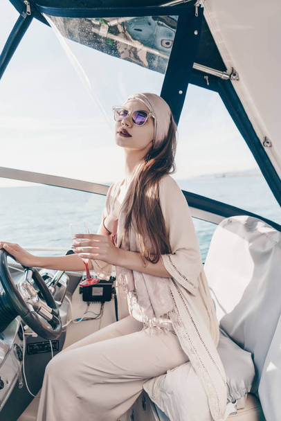 a luxurious stylish girl in sunglasses runs her yacht, sails the Caribbean sea and drinks champagne - Foto, afbeelding