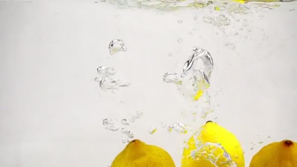 Video de limones en cámara lenta sobre fondo blanco. Los frutos amarillos maduros se sumergen en agua con burbujas
. - Imágenes, Vídeo