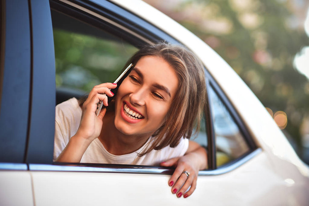 Beautiful woman with phone smiling while sitting on the back seat in the car. - Foto, immagini