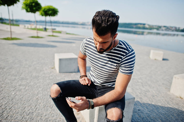 Handsome tall arabian beard man model at stripped shirt posed outdoor. Fashionable arab guy with mobile phone. - Photo, Image