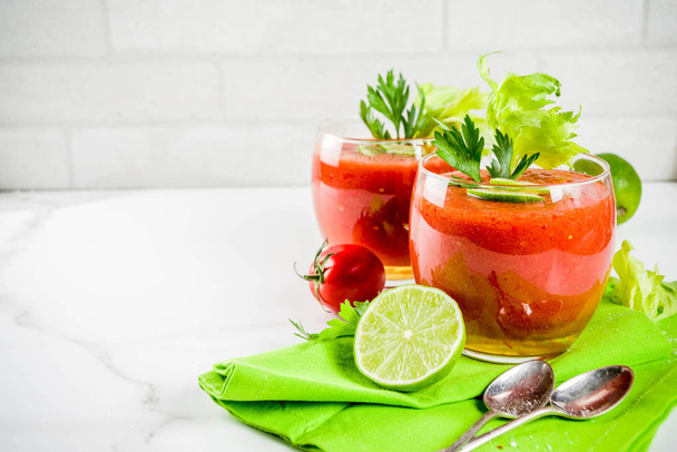 Summer veggie food, Cold soup gazpacho in glasses with with fresh celery, parsley and lime juice. White marble background copy space - Photo, Image