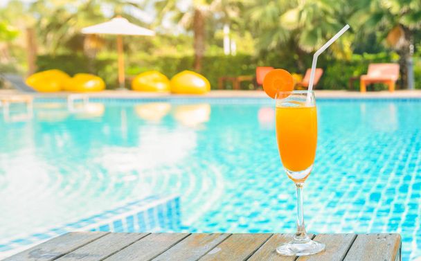 屋外スイミング プール、夏の熱帯休日の概念で木製のテーブルにカクテル グラスにニンジンのスライスとオレンジ ジュース - 写真・画像