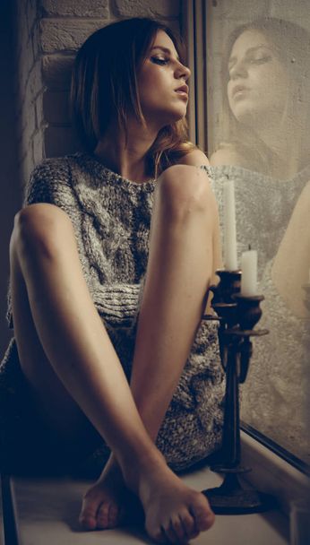 Young woman sitting on window and looking outside, lonely mood - Foto, imagen