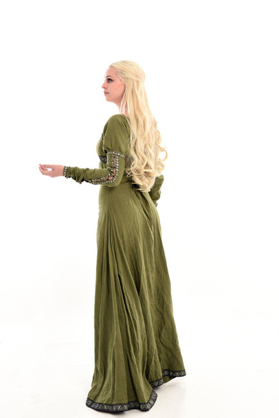 中世のグリーンのドレスを着ている金髪の女の子の完全な長さの肖像画。ホワイト スタジオの背景に分離カメラから離れて直面している立ちポーズ. - 写真・画像