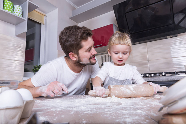 Fathers day! A tiny sweet girl with blond hair spends time with her dad, cooking in the kitchen. Preparations for the holidays. Baking. - Fotoğraf, Görsel