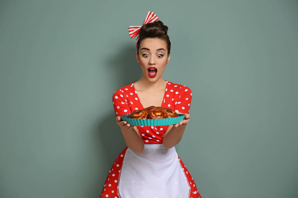Funny young housewife with homemade pastry on color background - Foto, afbeelding