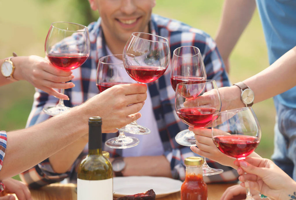 Νέοι άνθρωποι με ποτήρια κρασί στο τραπέζι σε εξωτερικούς χώρους. Το καλοκαίρι μπάρμπεκιου - Φωτογραφία, εικόνα