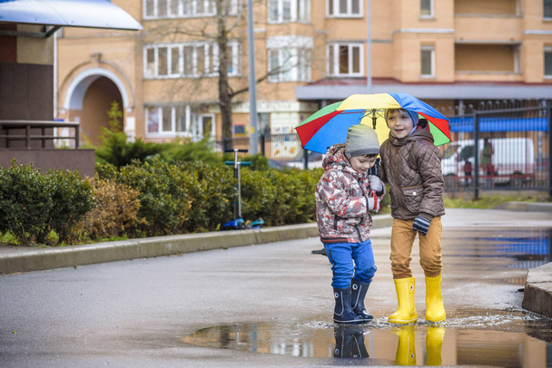 Dois meninos, agachados numa poça, com guarda-chuvas. conceito de comunicação amizade
 - Foto, Imagem