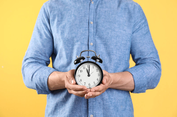 Young man holding clock on color background. Time management - Foto, afbeelding