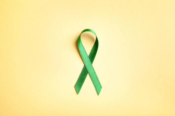 Green ribbon on color background, top view. Cancer awareness - Foto, afbeelding