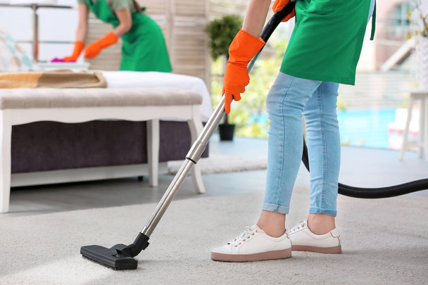 Woman removing dirt from carpet with vacuum cleaner in bedroom - Valokuva, kuva